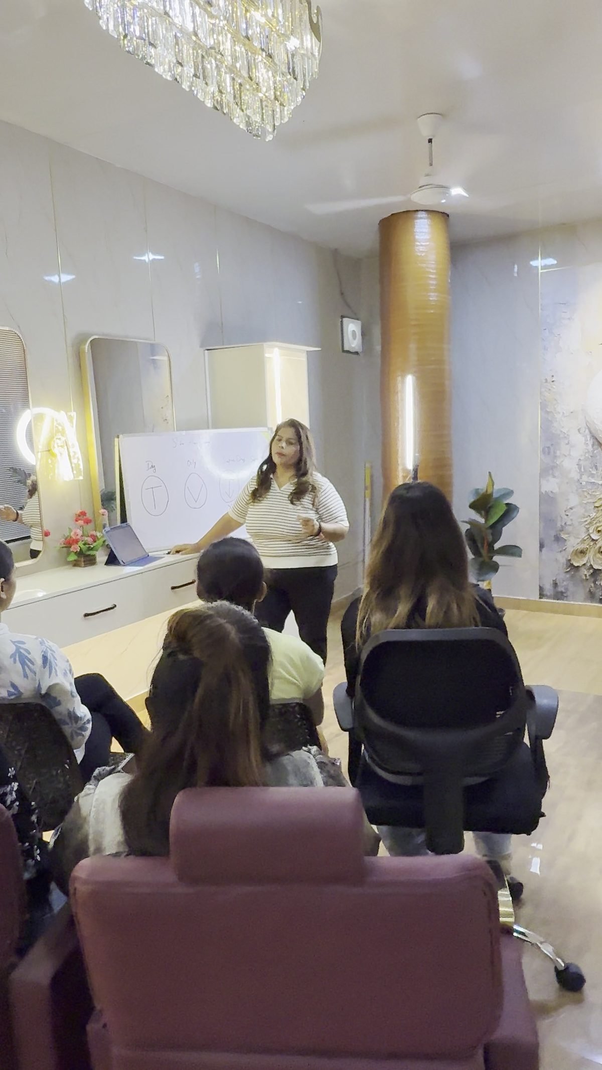 A class in progress: Bharti at the whiteboard while students sit in the studio’s maroon styling chairs.