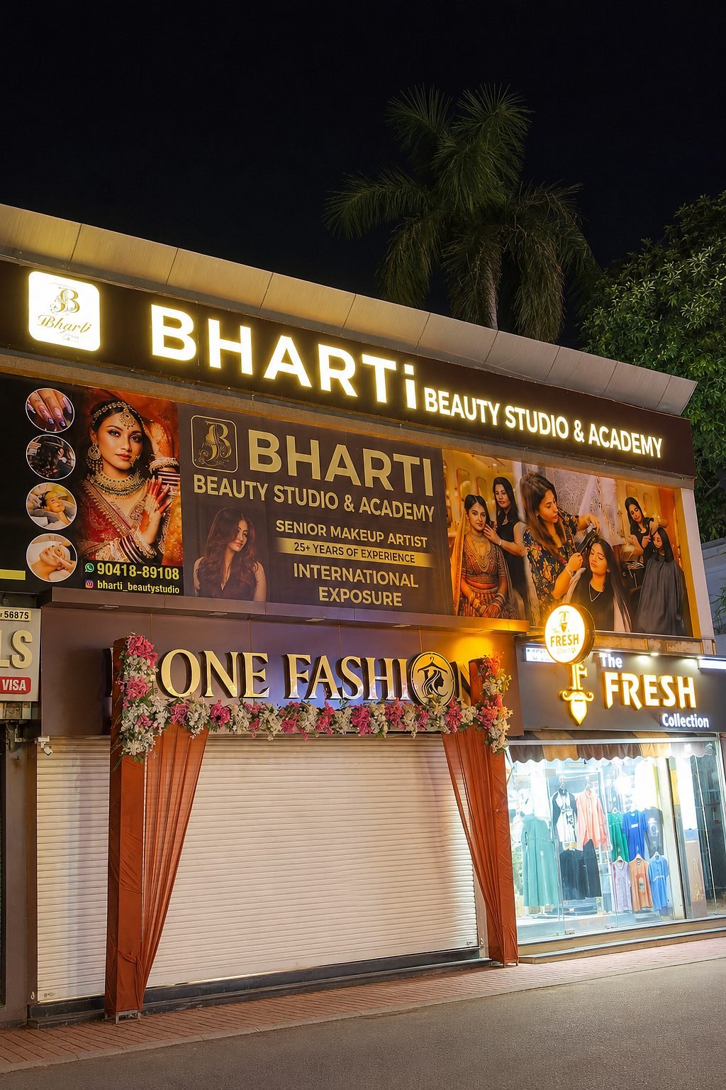 The building at night from across the street, the lit Bharti board above the shopfronts.