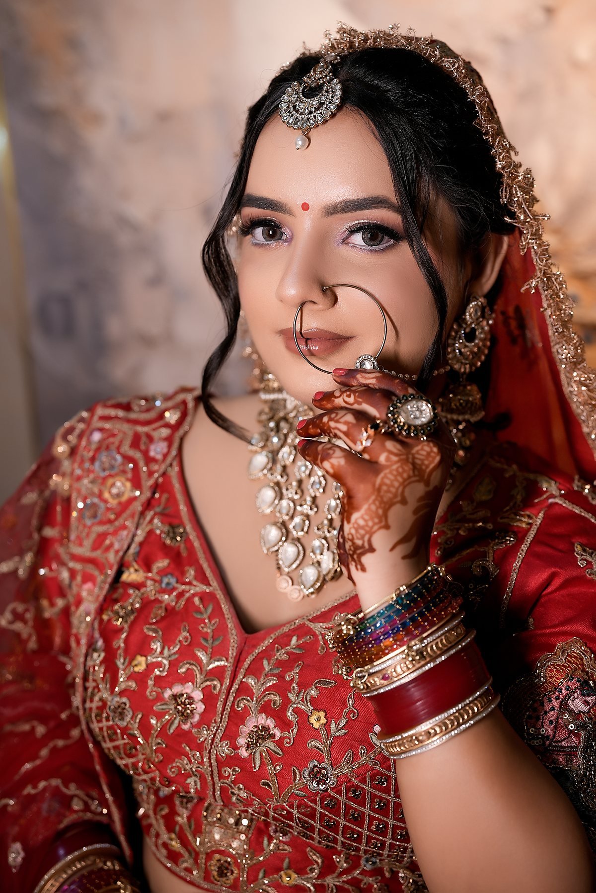 A bride looking to camera, mehndi on her raised hand, kundan and red silk.