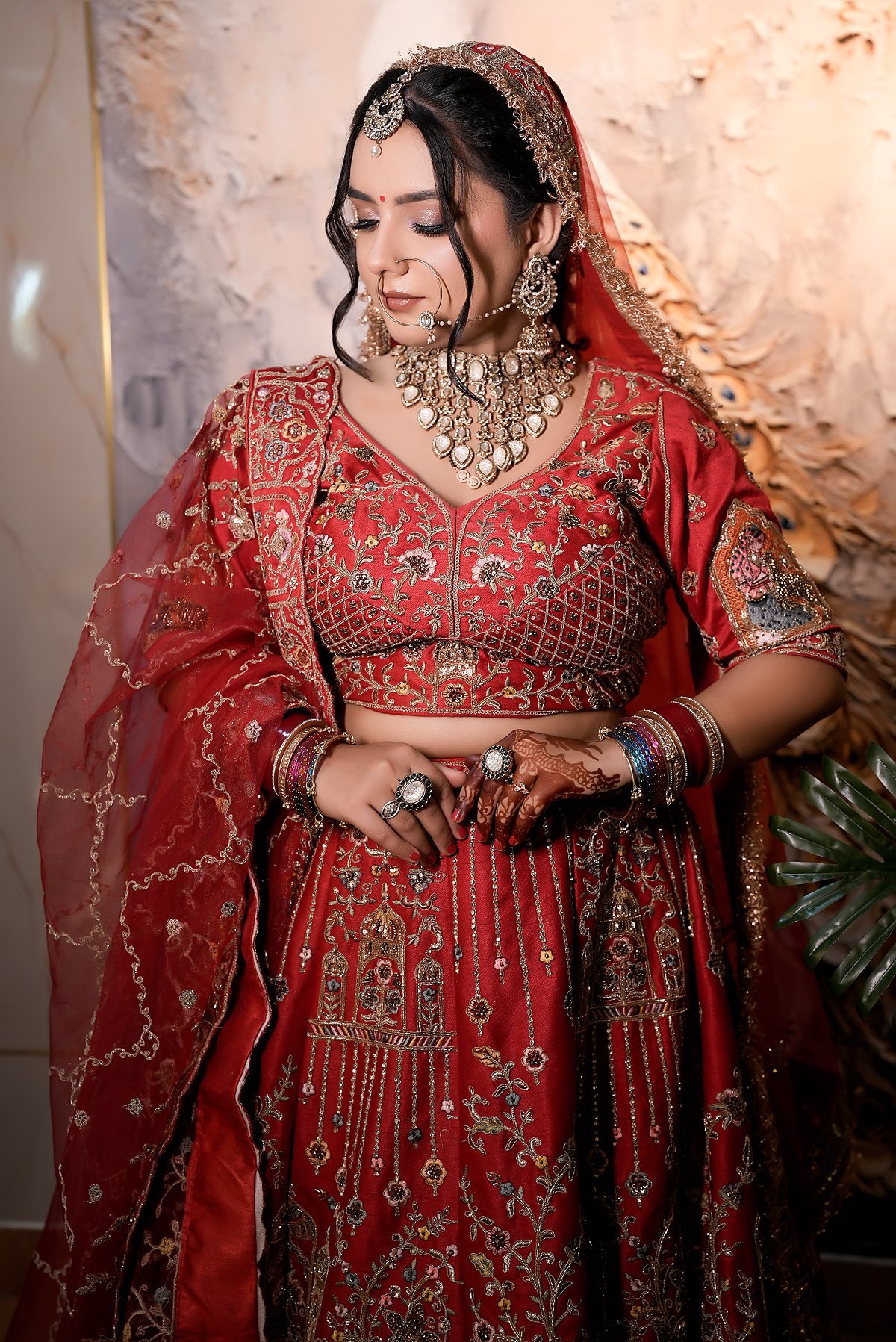 A bride in a red embroidered lehenga with kundan jewellery, full length.