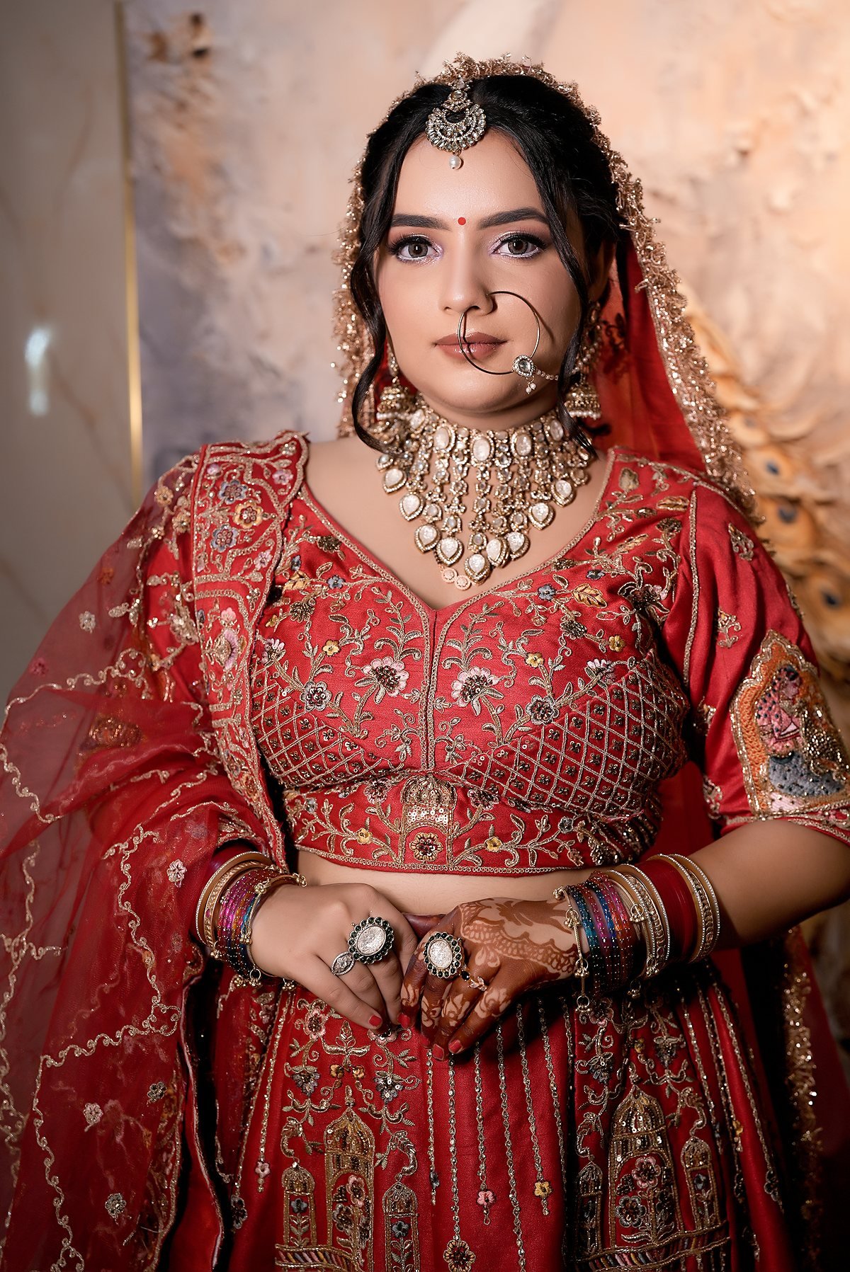 A bride's hands with mehndi, chooda and rings, against red embroidery.