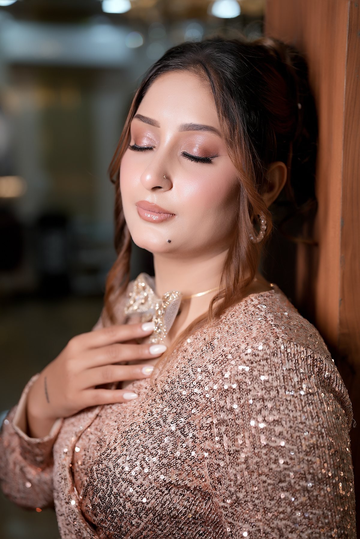 A client in a champagne sequin outfit, softly lit, hand at her chest.