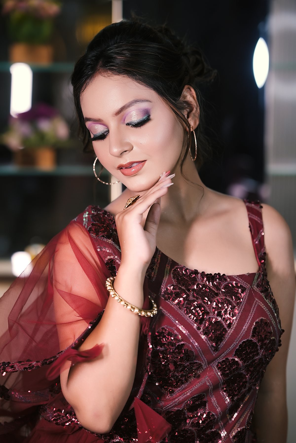 A client in a wine-coloured gown, sculpted cheekbone and gold jewellery.