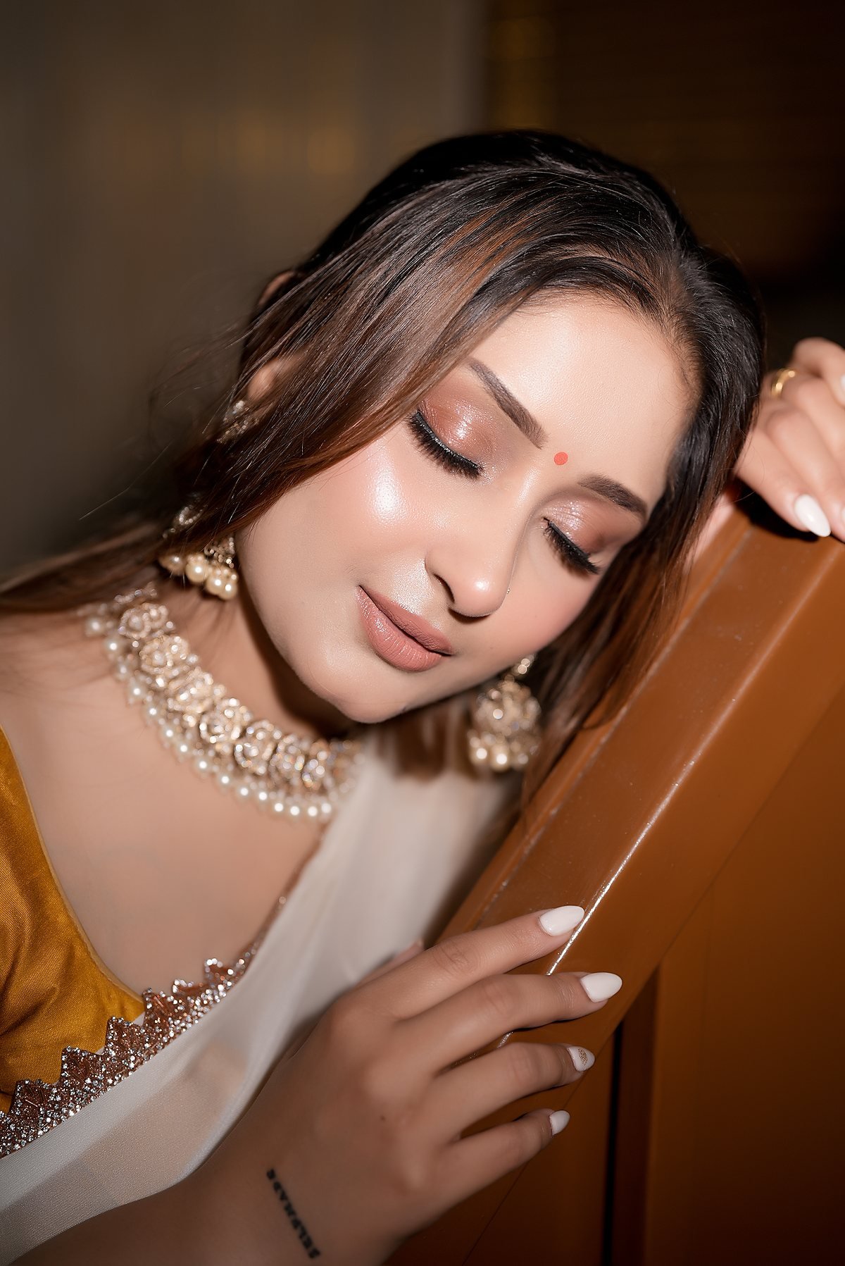 A client in an ivory saree and kundan necklace, classic natural makeup.